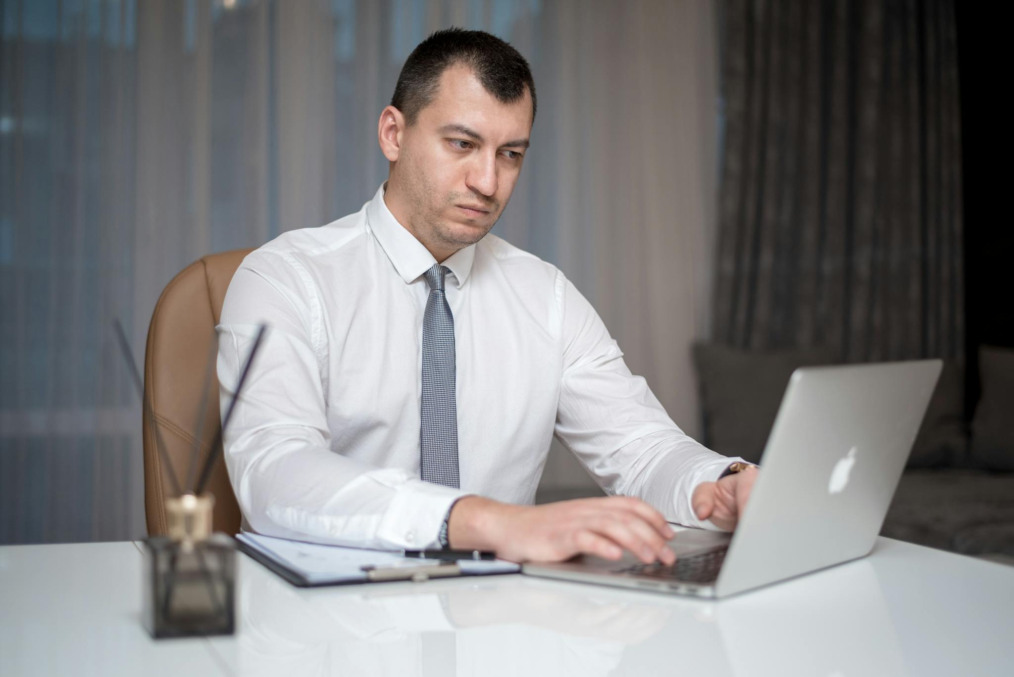 Professional businessman wearing a white shirt working on a laptop at an office desk indoors.